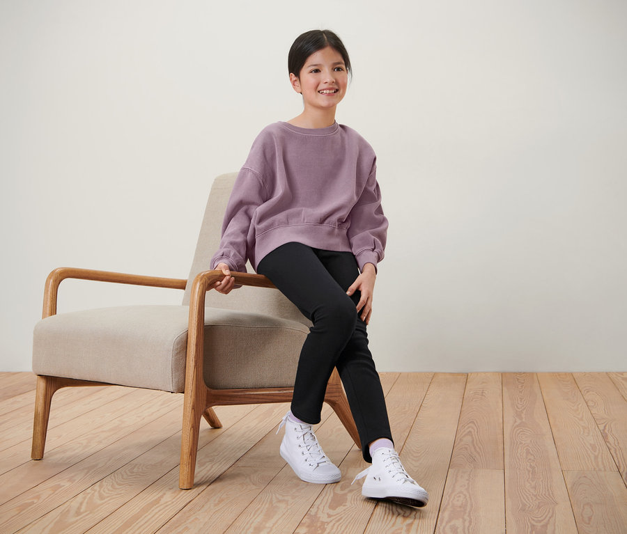 Fille assise sur une chaise portant un legging thermique pour enfant noir.