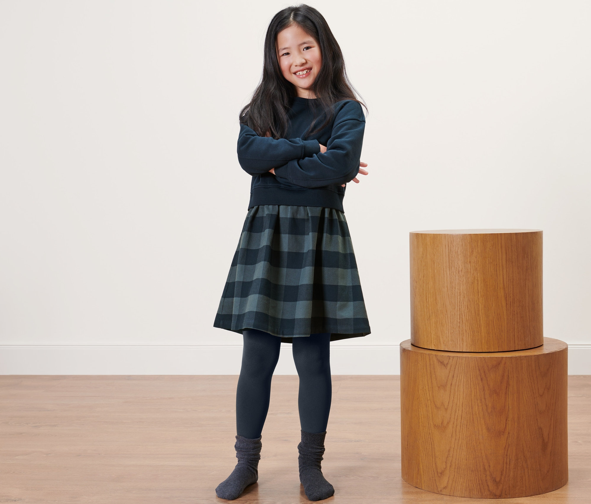 Une fille souriante se tient debout, les bras croisés, portant un legging thermique pour enfant, une robe et un pull.