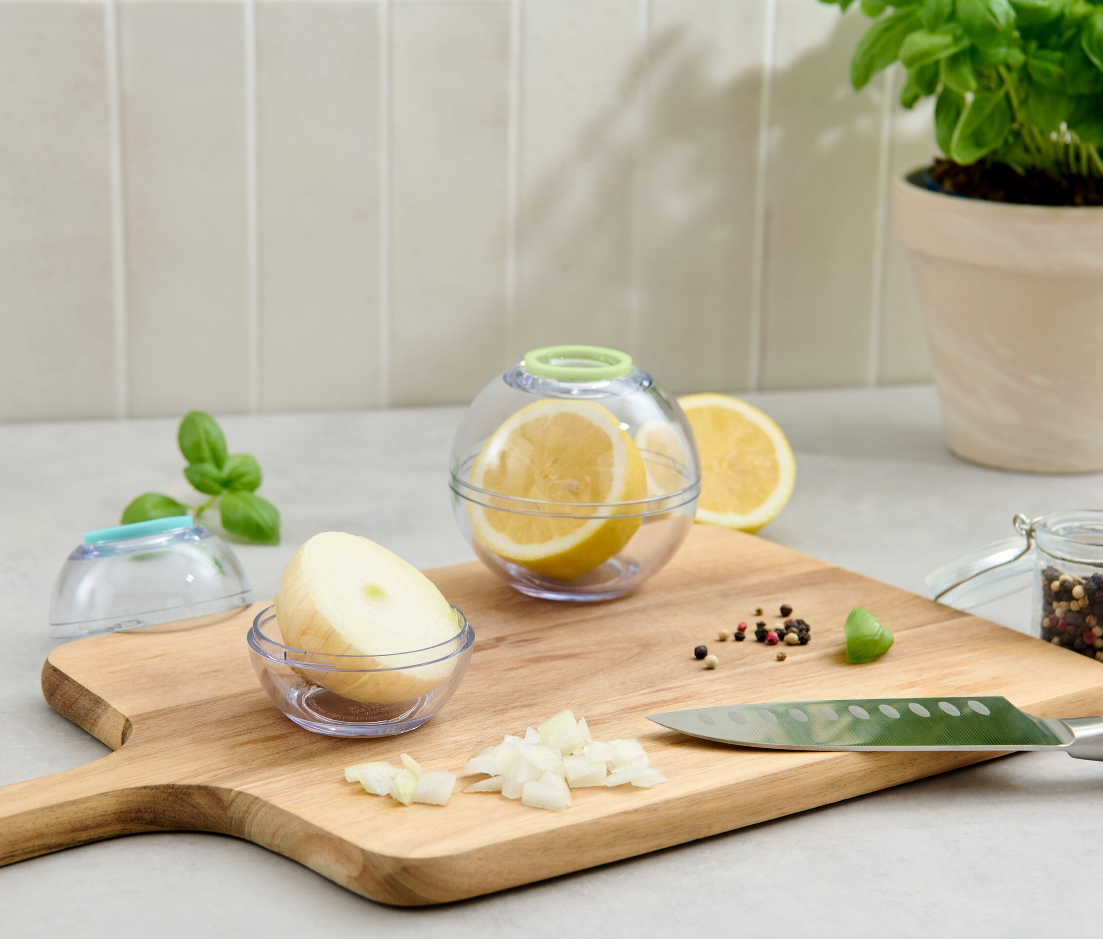 Deux boîtes fraîcheur en forme de boule, une avec un citron, l'autre avec un oignon, sont posées sur une planche à découper.