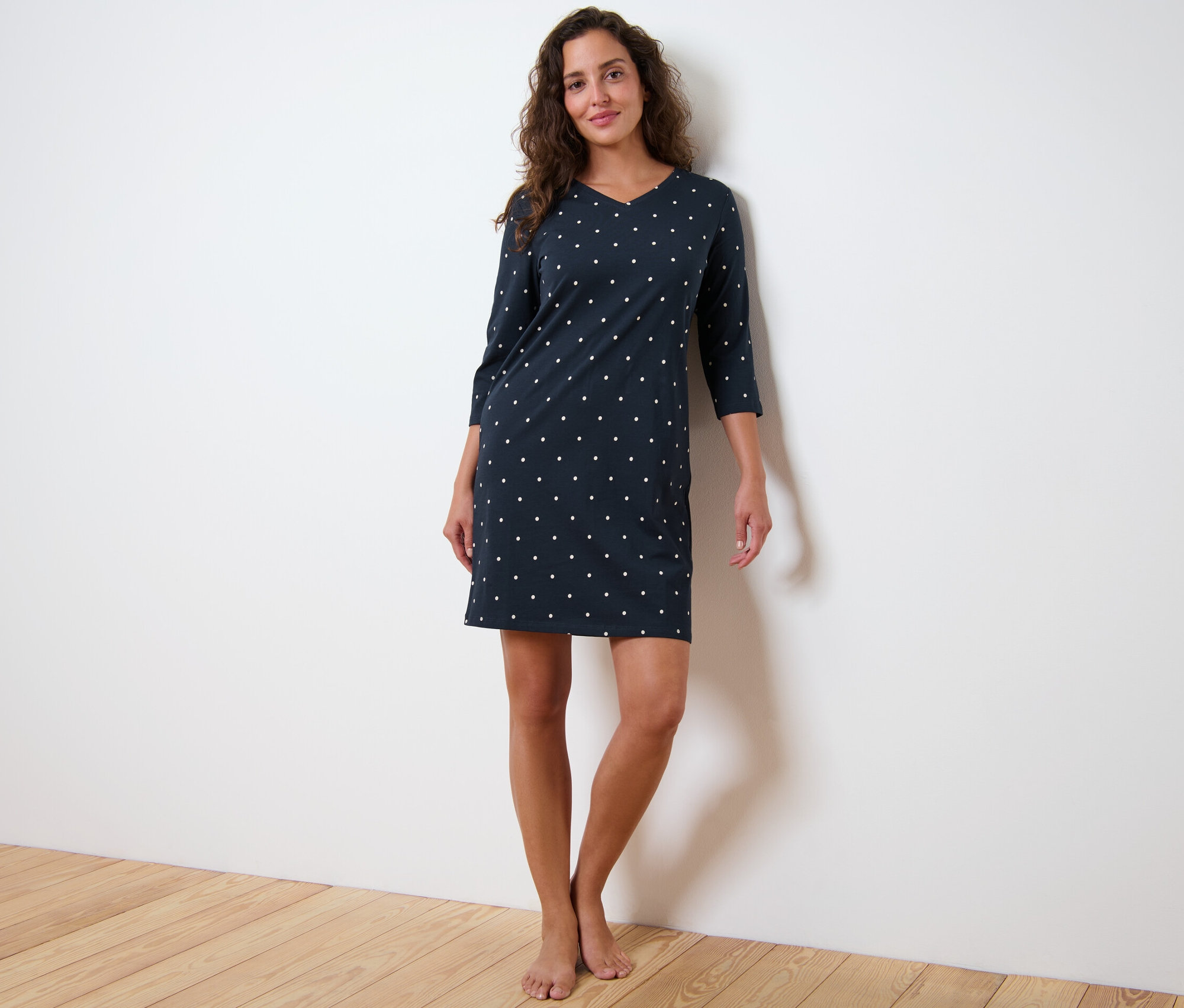 Une femme debout portant une chemise de nuit à manches trois-quarts à pois.