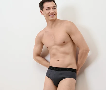 Un homme souriant pose en 3 slips gris.