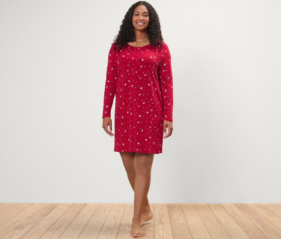 Une femme debout souriant à la caméra portant une chemise de nuit rouge.