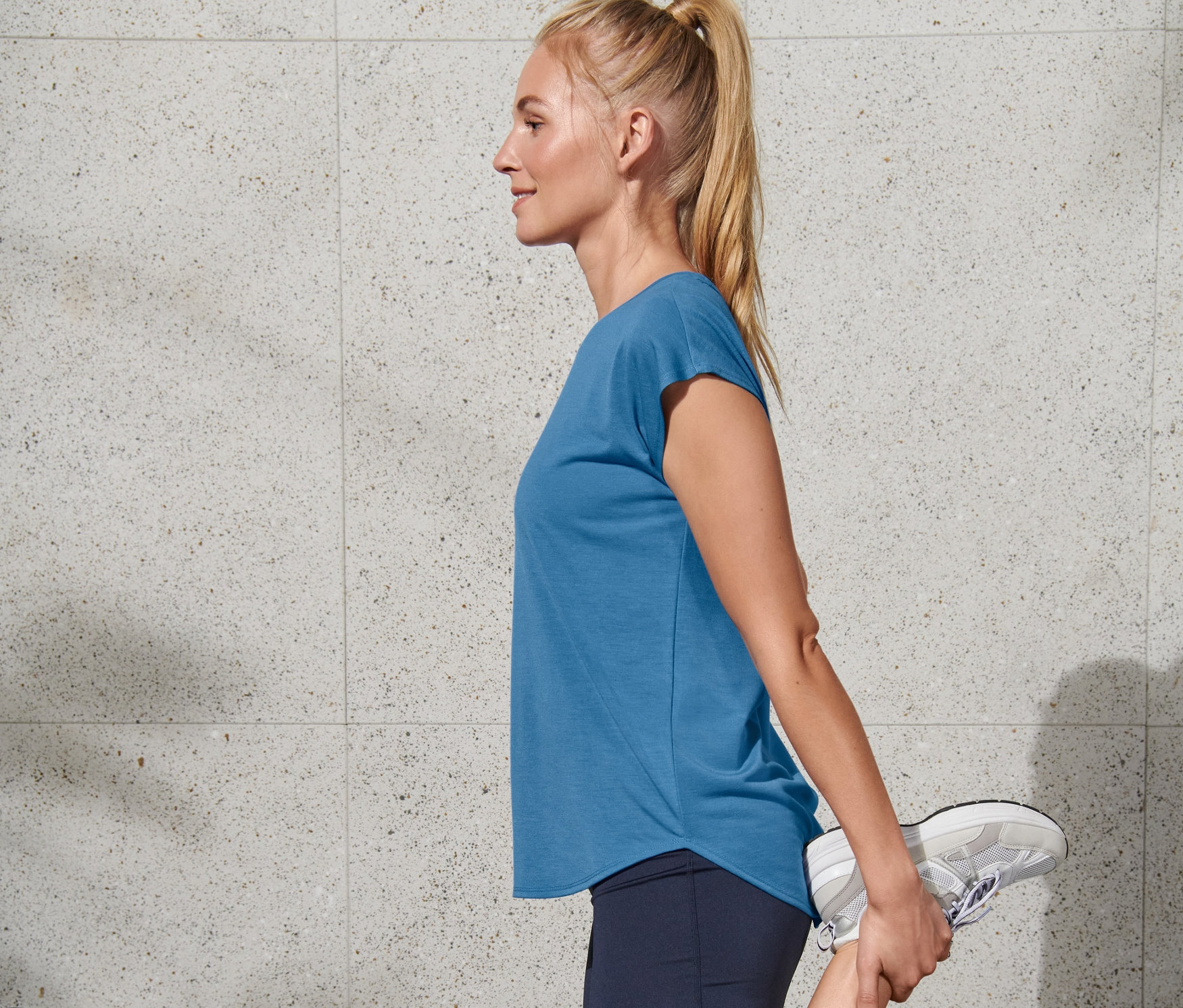 Blonde étire sa jambe, portant un t-shirt de sport bleu Regatta.