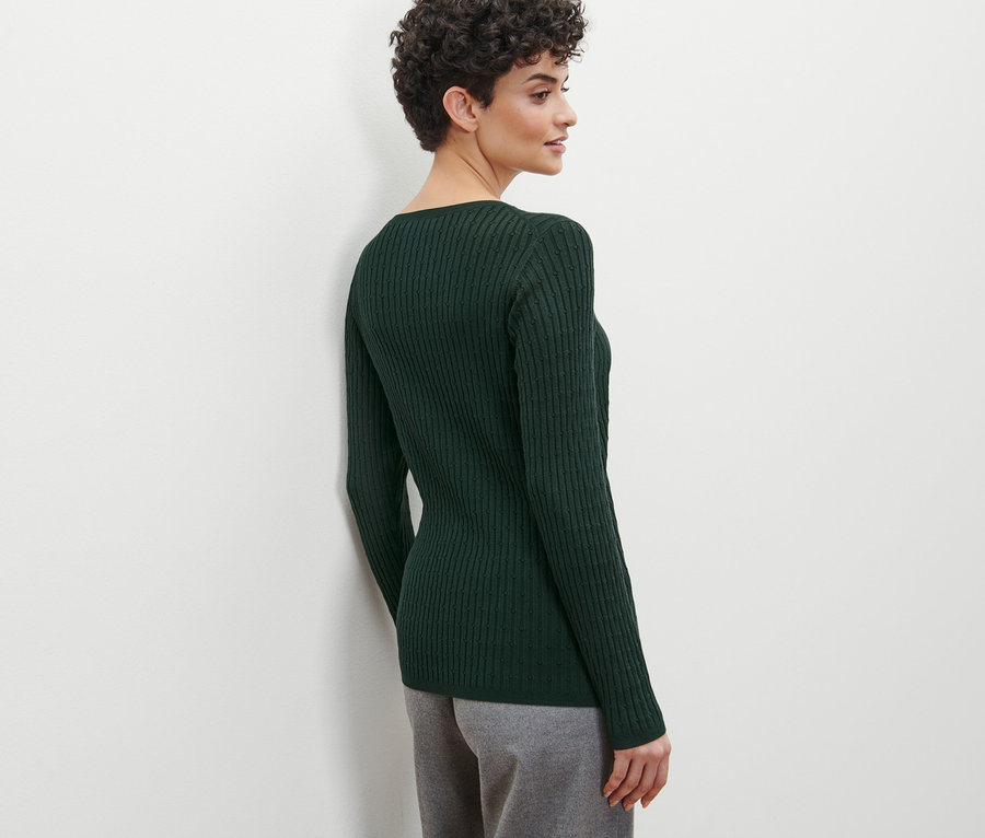 Femme de profil portant un pull en maille torsadée vert.