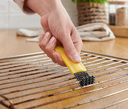 Une femme nettoie une grille de four avec une brosse à four avec racloir.
