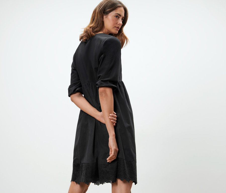 Femme posant dans une robe tissée noire avec broderie.