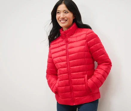 Femme souriant et posant dans une veste matelassée rouge.