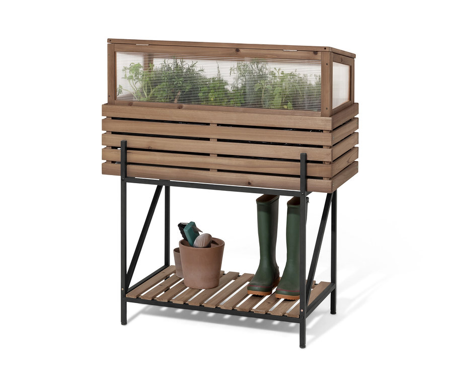 Une jardinière surélevée avec serre châssis « Elin » avec des plantes, un pot et des bottes en caoutchouc.