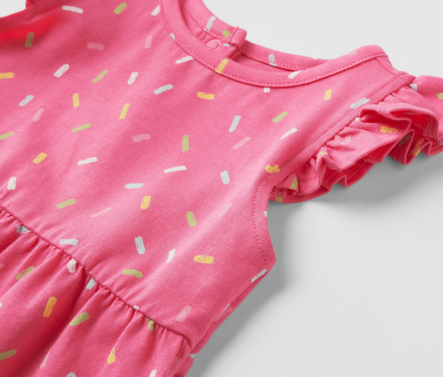 Gros plan sur une robe en jersey rose pour enfant, ornée d'un motif de vermicelles multicolores.