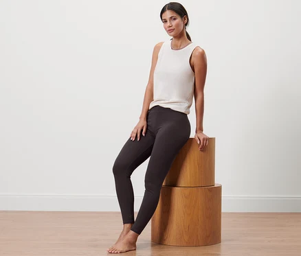 Femme assise sur des cylindres en bois portant un legging de sport et un débardeur.