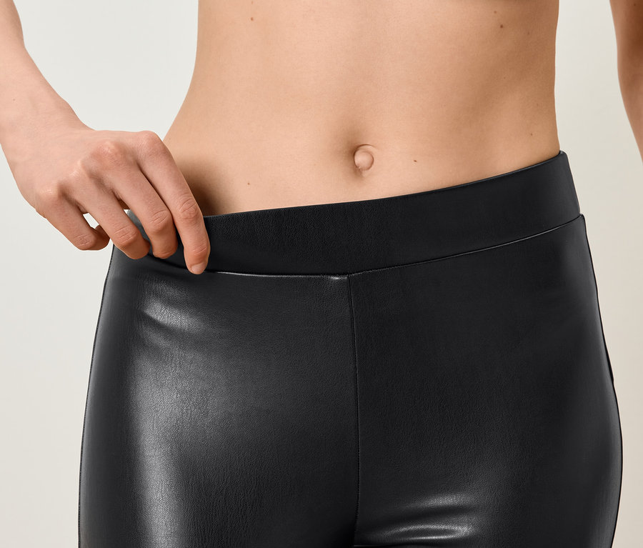 Gros plan d'une femme tenant la taille d'un legging en similicuir noir.