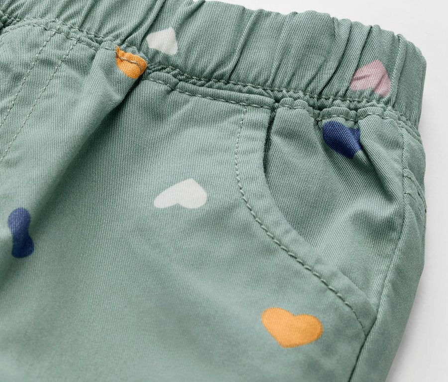 Détail d'un pantalon enfant à enfiler - Coupe « Ella », vert pastel, avec des cœurs colorés.