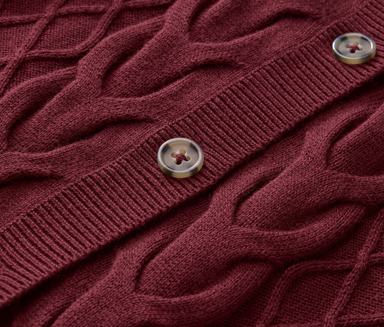 Gros plan sur un pull tricoté bordeaux avec un motif de torsades et deux boutons.