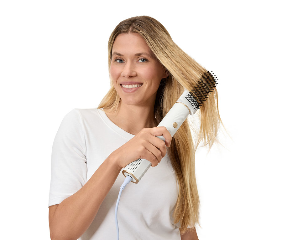 Une femme se coiffe les cheveux blonds avec une brosse soufflante.