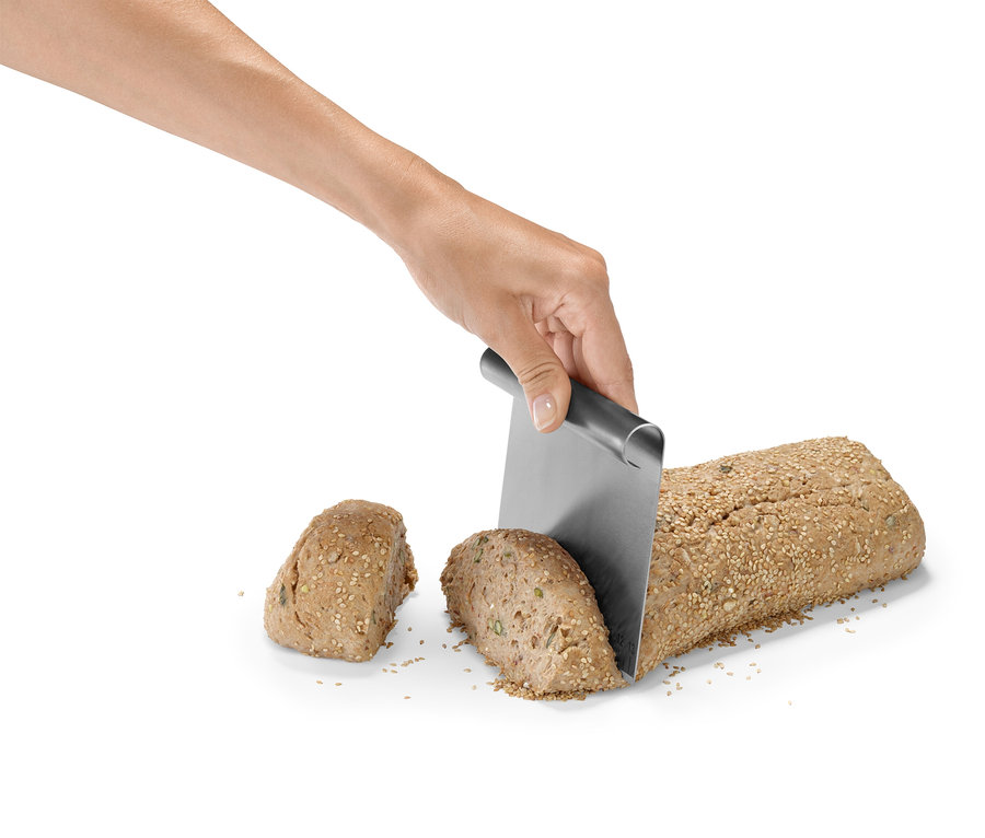 Une main coupe une miche de pain saupoudrée de graines avec un couteau en métal.