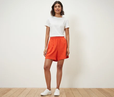 Une femme debout portant un short en lin orange et un t-shirt blanc.