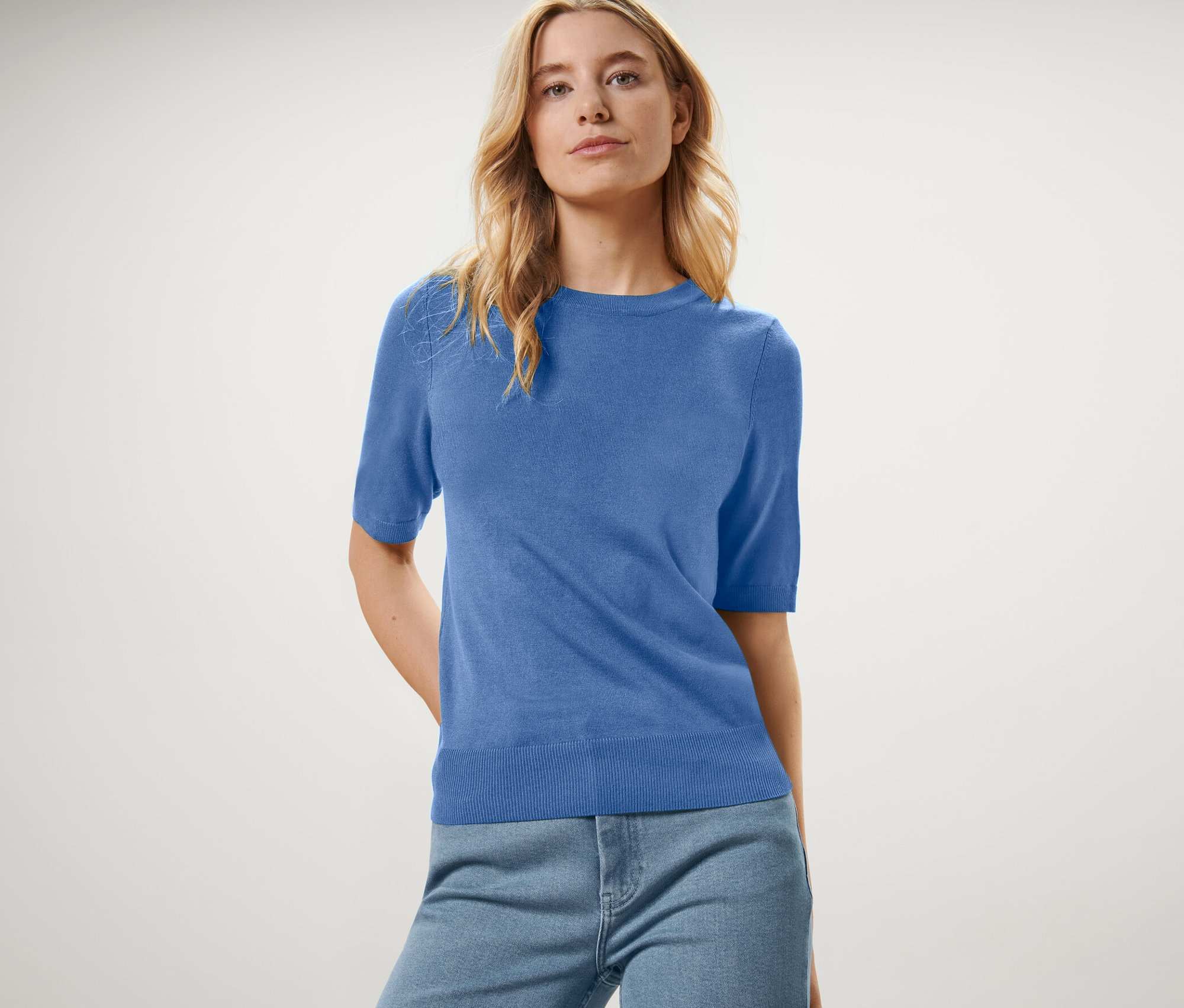 Femme portant un pull bleu en maille fine et un jean.