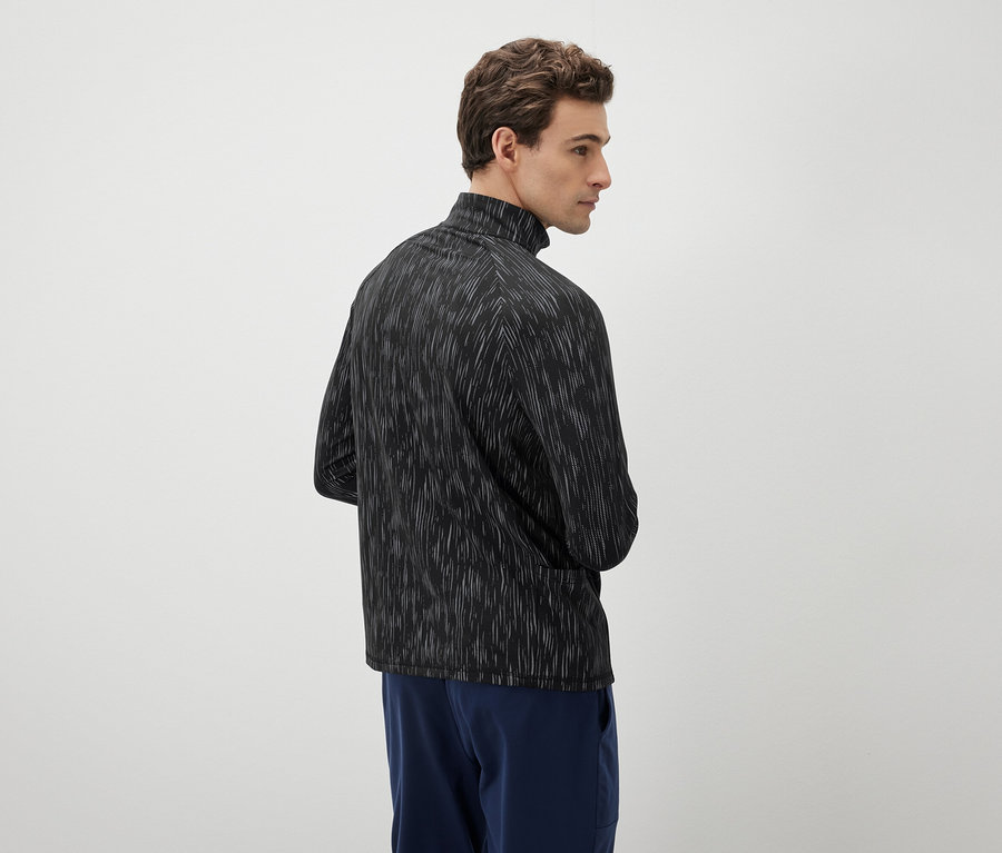 Un homme regarde vers la gauche et porte un haut noir et blanc et un pantalon bleu.