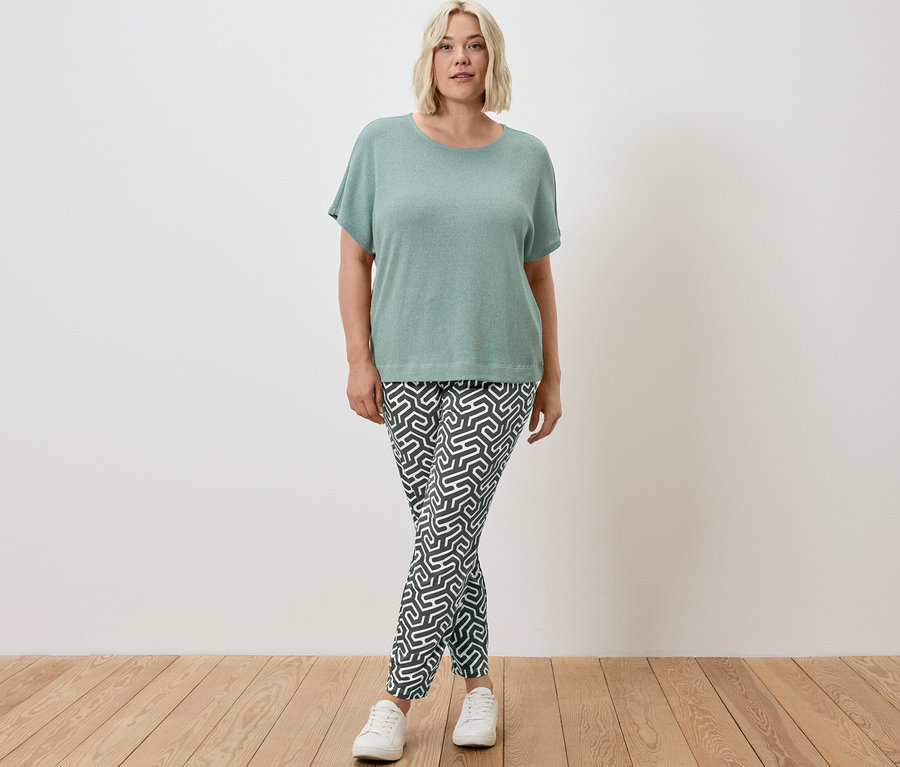 Une femme debout portant un t-shirt structuré sauge et un pantalon en jersey imprimé vert.