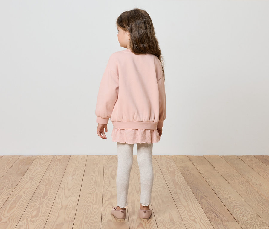 Une fille se tient dos à la caméra, vêtue d'un sweat-shirt rose, de leggings blancs et de chaussures roses.