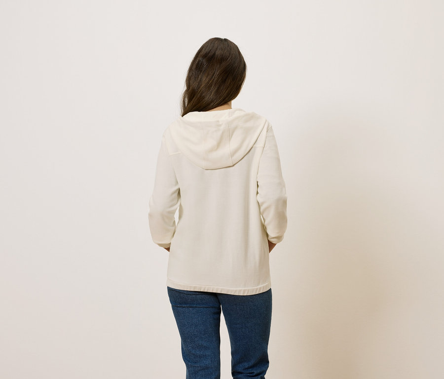 Vue de dos d'une femme aux cheveux bruns portant un sweat à capuche crème et un jean bleu.