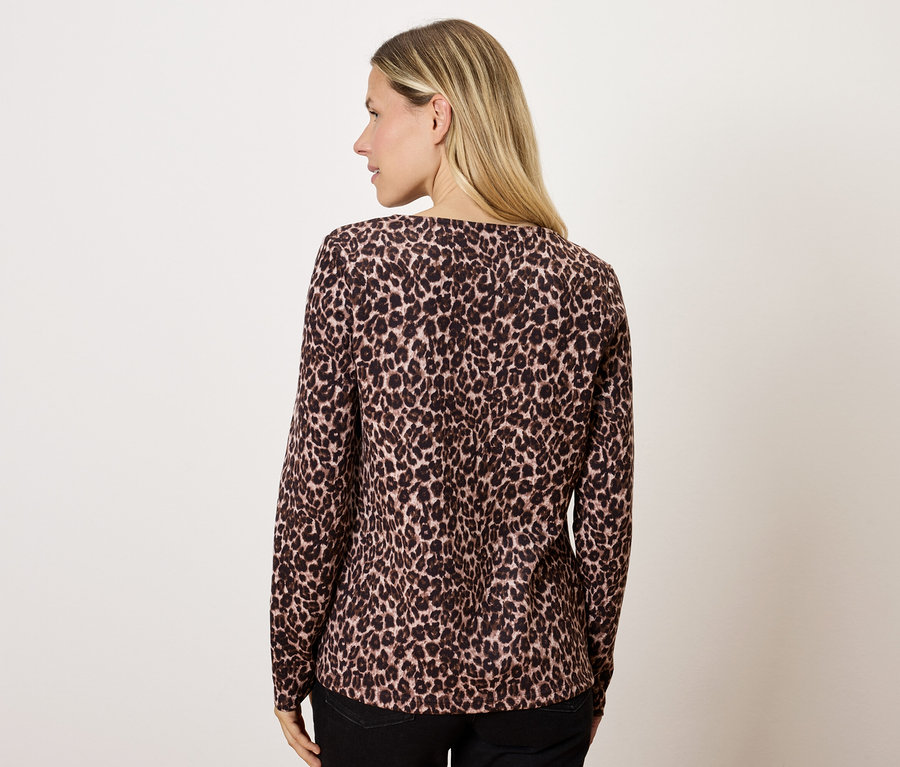 Blonde portant un chemisier marron à motif animalier, dos à la caméra.