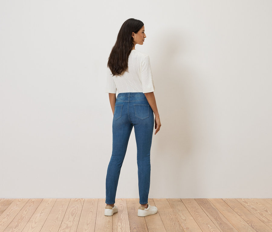 Une femme se tient dos à la caméra, portant un jean bleu, un haut blanc et des baskets blanches.