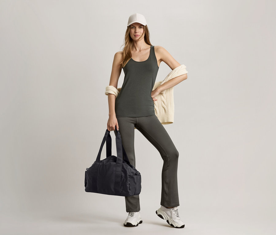 Femme portant un haut vert olive, un pantalon de sport modelant et tenant un sac de sport noir.