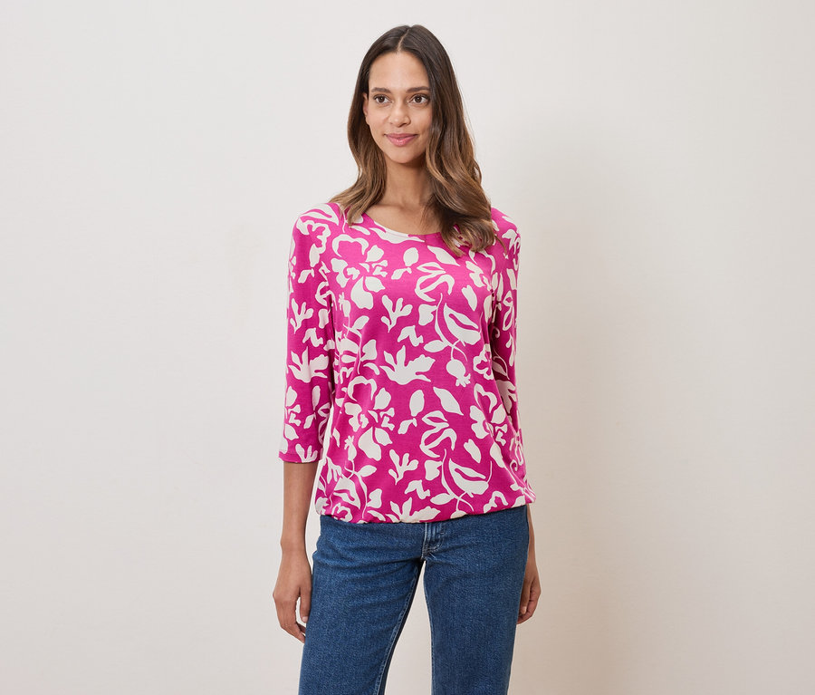 Femme portant un haut rose à motifs floraux et un jean.