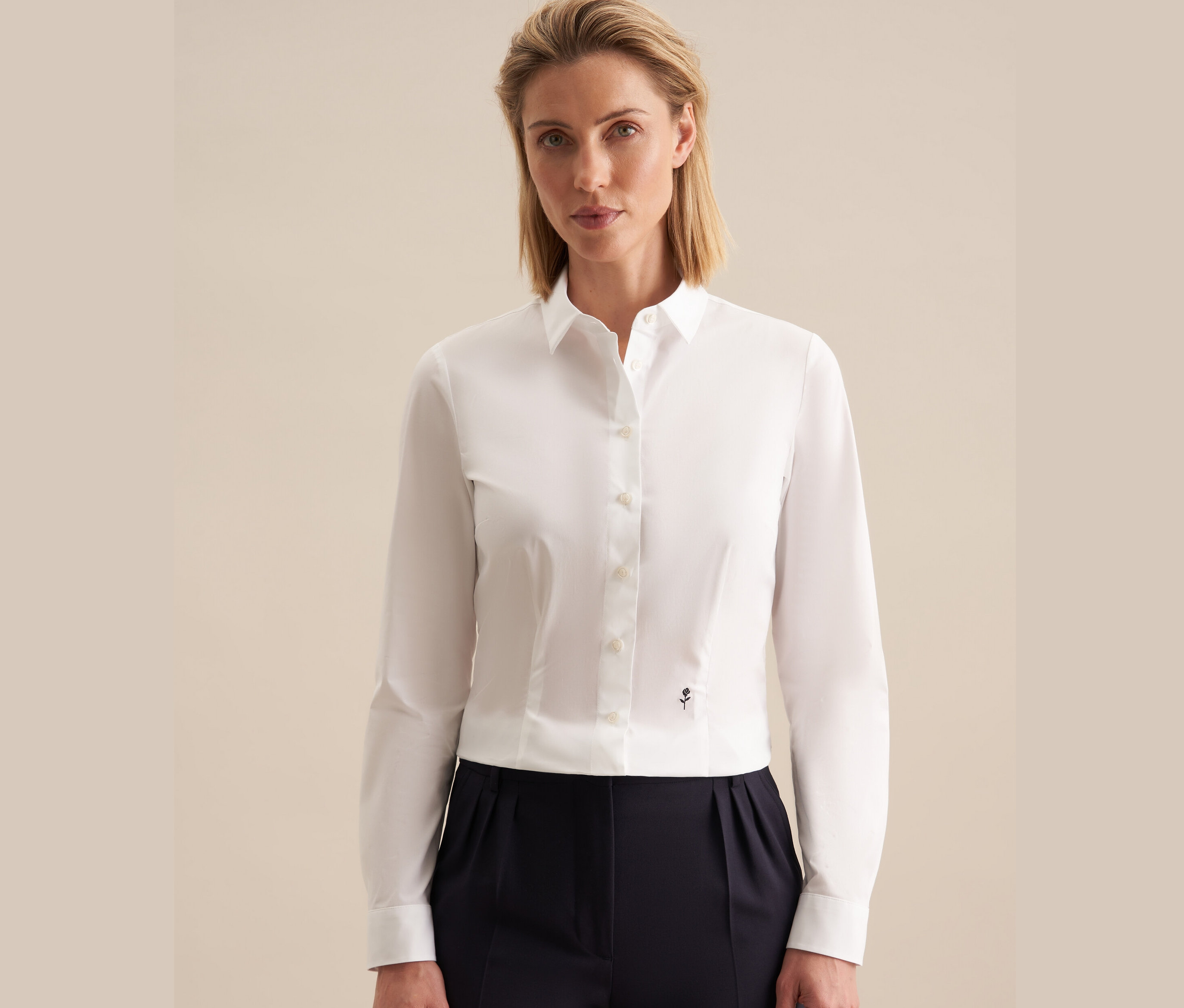 Une femme porte une chemise blanche Seidensticker Slimfit et un pantalon bleu marine.