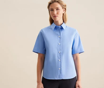 Femme portant un chemisier à manches courtes Seidensticker bleu clair et un pantalon foncé.