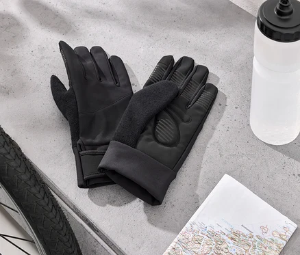 Deux gants de cyclisme noirs sont posés à côté d'un pneu de vélo, d'une bouteille d'eau blanche et d'une carte sur une surface grise.