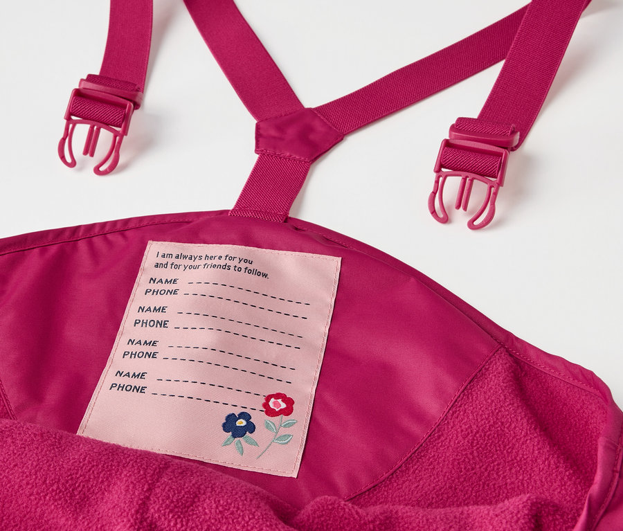 Détail du pantalon de pluie thermique pour enfant, baie, avec bavette et étiquette de nom.