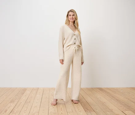 Une femme blonde se tient debout sur un plancher de bois en cardigan et pantalon crème.