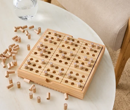 Jeu en bois avec des chevilles sur une table à côté d'un verre d'eau.