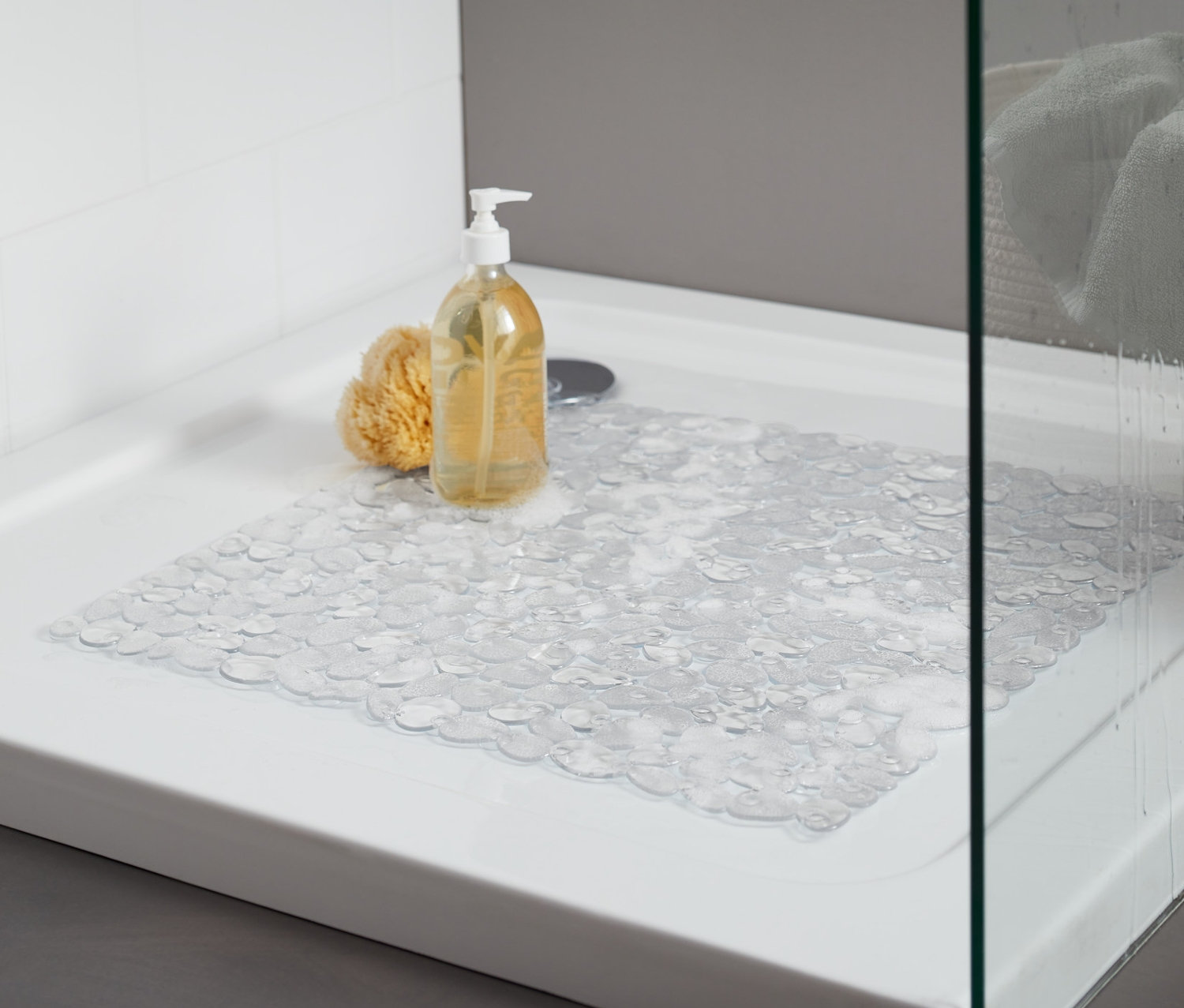 Receveur de douche avec un tapis de douche transparent. Sur le receveur se trouvent une éponge de bain jaune et un flacon avec pompe.