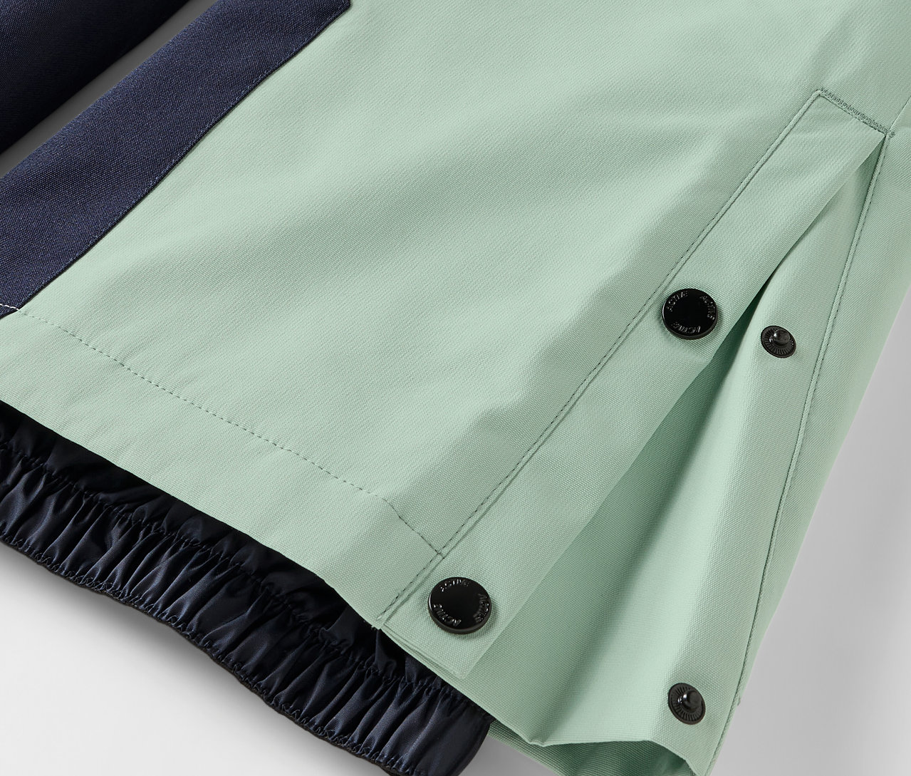 Détail d'un pantalon vert clair avec fermeture à boutons et ourlet élastique.