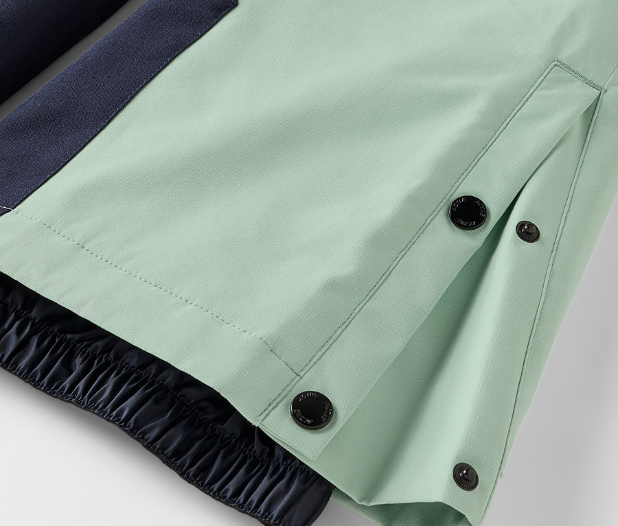 Détail d'un pantalon vert clair avec fermeture à boutons et ourlet élastique.