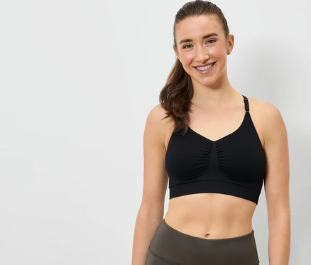Une femme souriante porte un soutien-gorge de sport noir et un legging gris.