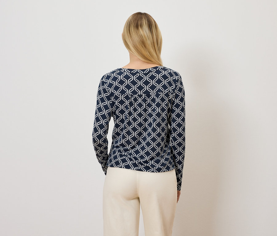 Une femme, de dos, porte un T-shirt à manches longues bleu marine avec un motif géométrique et un pantalon beige.