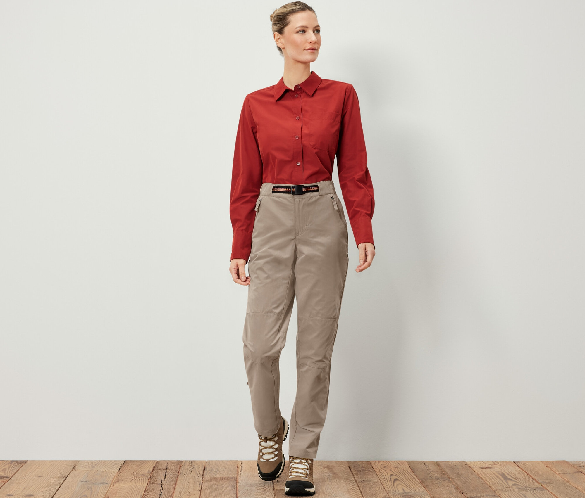 Une femme porte un pantalon d’extérieur avec protection anti-moustiques, une chemise marron et des chaussures de randonnée.