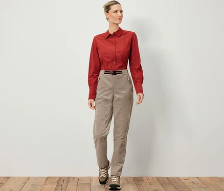 Une femme porte un pantalon d’extérieur avec protection anti-moustiques, une chemise marron et des chaussures de randonnée.