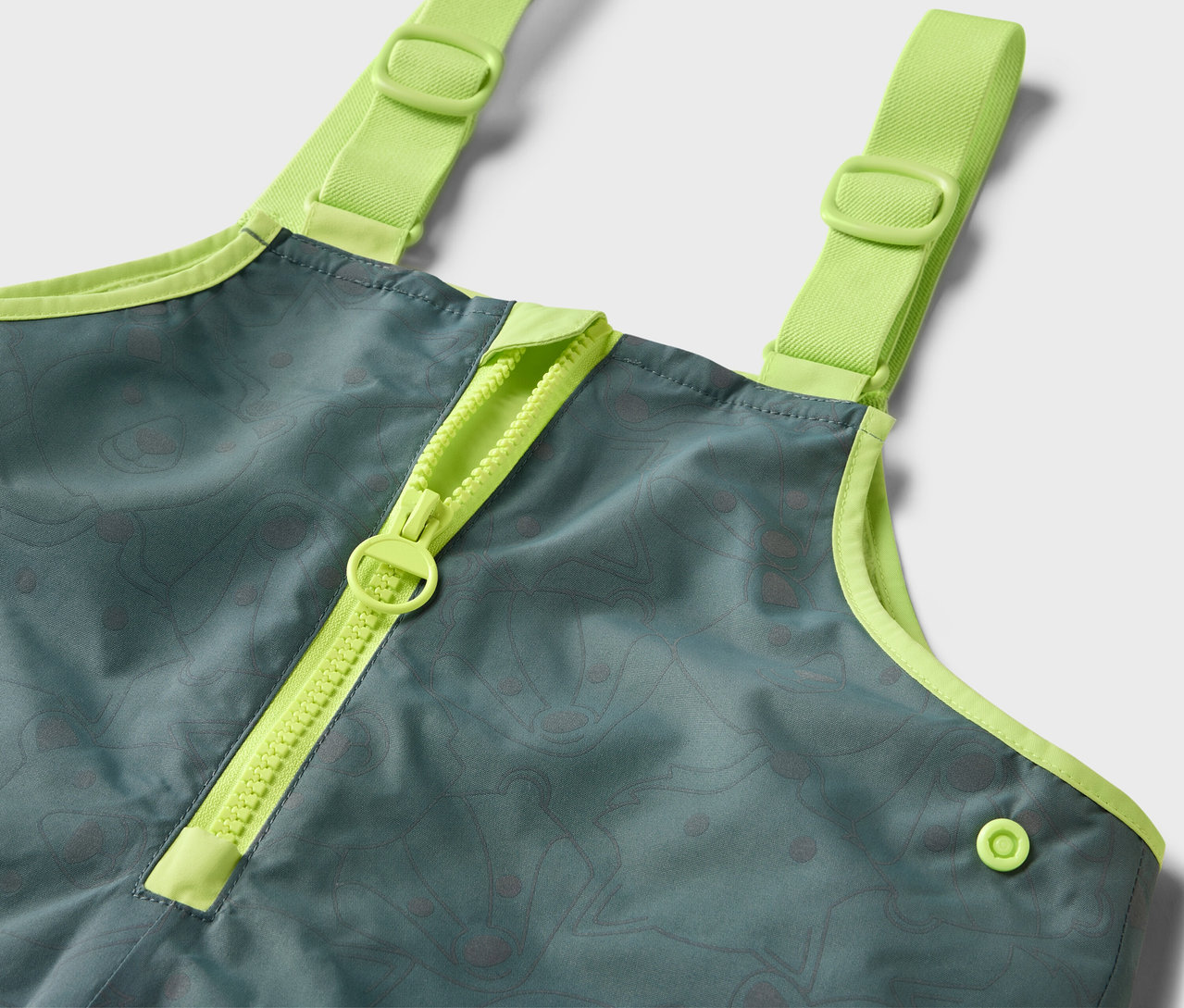 Détail d'un pantalon de pluie thermique pour enfants avec des éléments réfléchissants, avec une fermeture éclair et des bretelles vert néon.