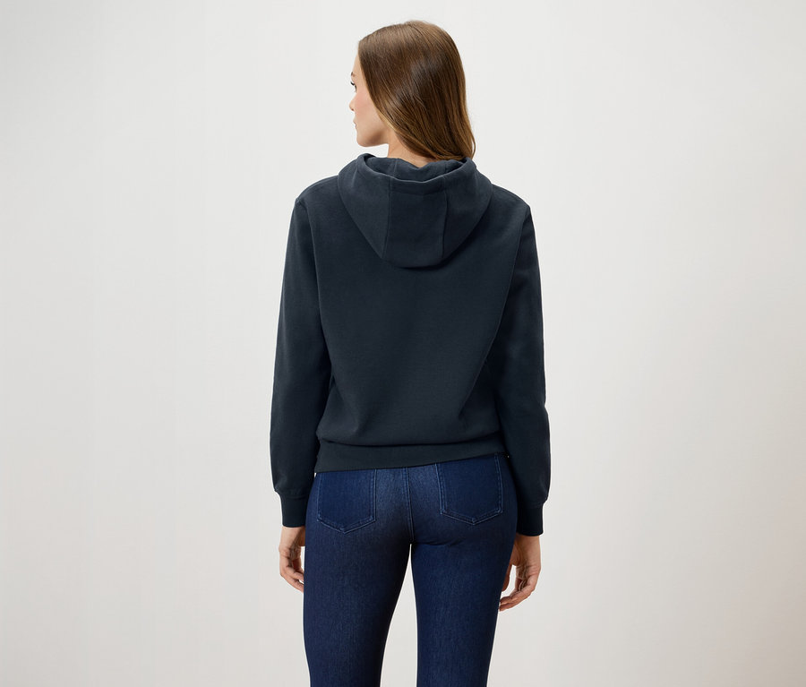 Une femme, vue de dos, porte un sweat à capuche bleu marine et un jean.