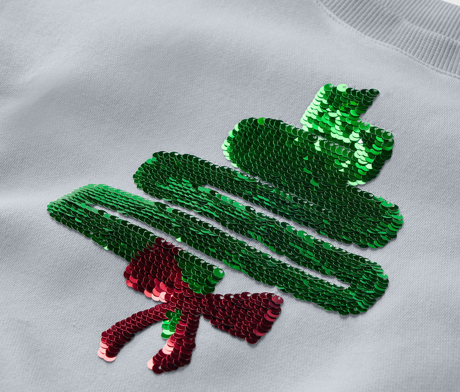 Détail d'un sweat-shirt gris avec un sapin de Noël à paillettes.