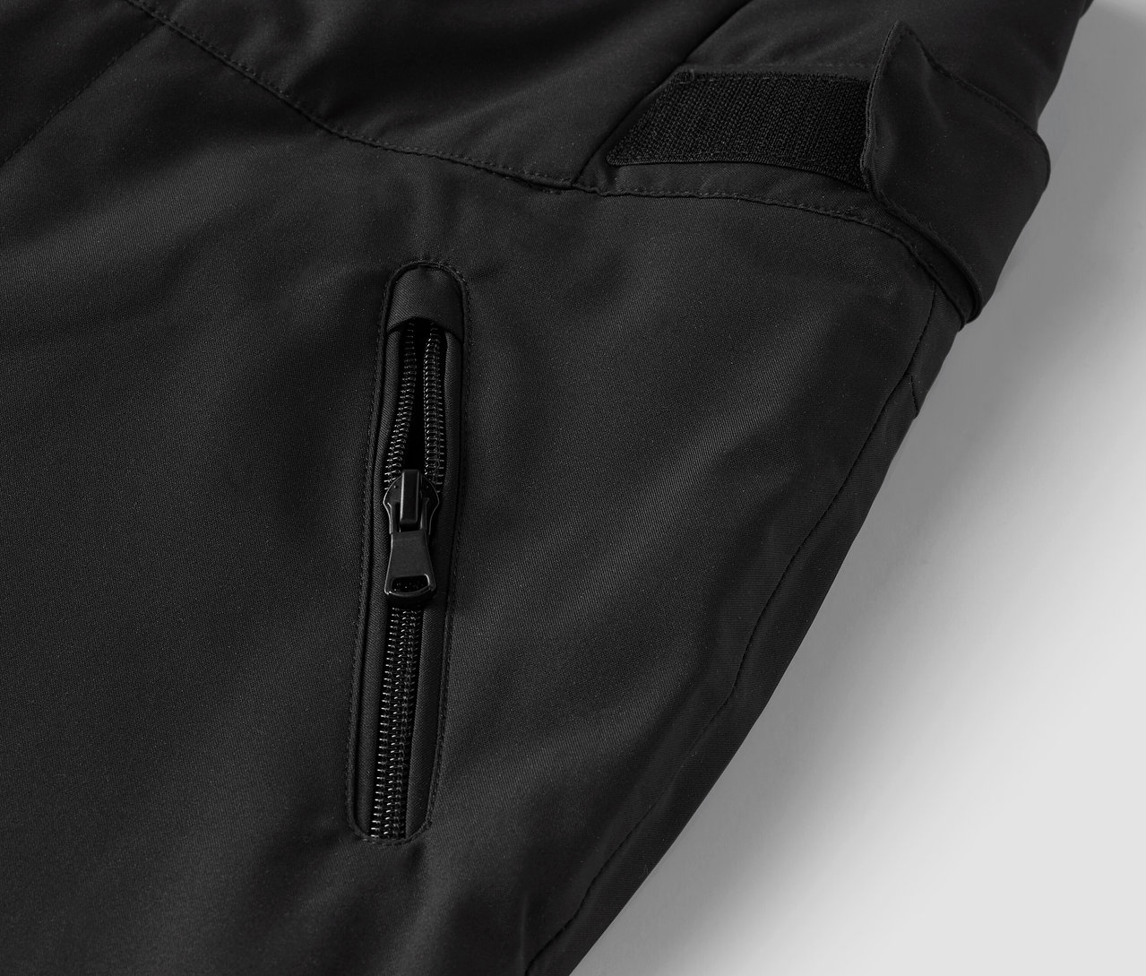 Détail d'un pantalon noir avec une poche zippée.