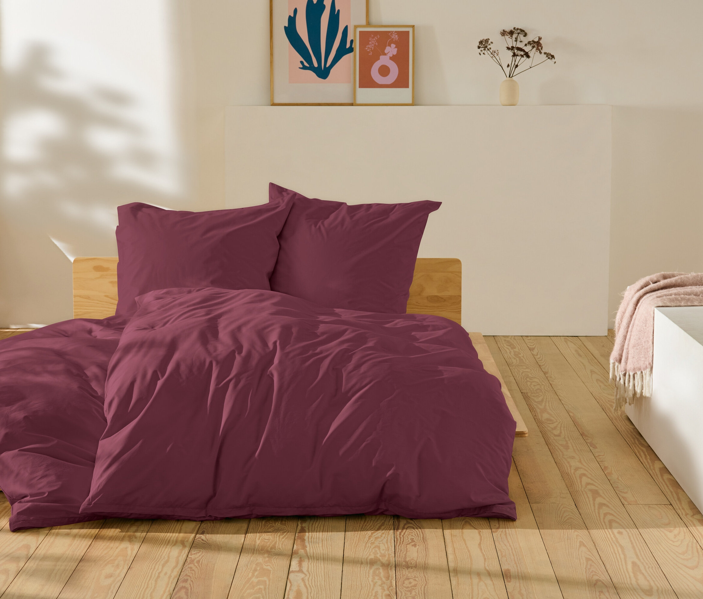 Du linge de lit bordeaux posé sur un lit sur un plancher en bois.