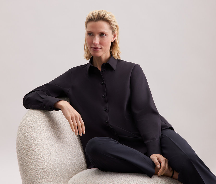 Une femme assise dans un fauteuil portant une chemise noire et un pantalon.