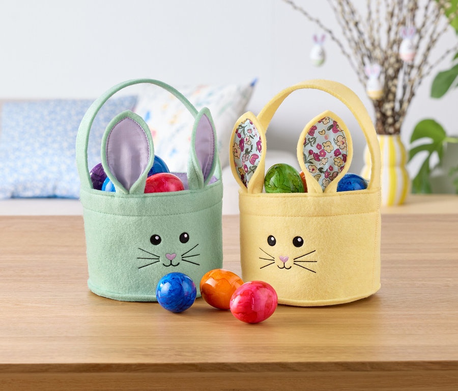 Deux paniers de Pâques en forme de lapin, un vert menthe et un jaune, remplis d'œufs colorés, sont posés sur une table.