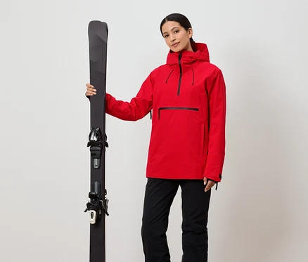 Femme tenant des skis en veste rouge et pantalon noir.